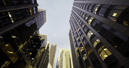 A stunning view of towering skyscrapers reaches towards a pale evening sky. The muted glow from...