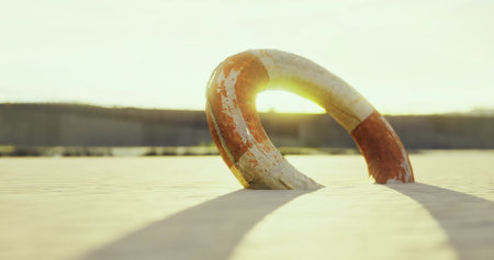 A brightly colored lifebuoy lies on the sandy beach, its paint worn from time. Soft sunlight bathes the scene in a warm glow, creating a serene atmosphere at dusk.の写真素材