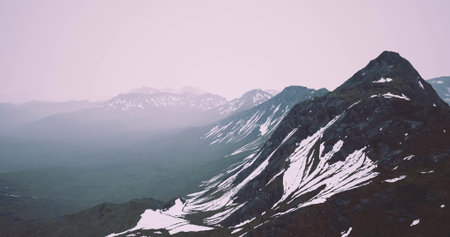 Breathtaking view of towering mountains blanketed with snow, shrouded in mist during early morning hours, creating an ethereal and tranquil environment in nature.の写真素材