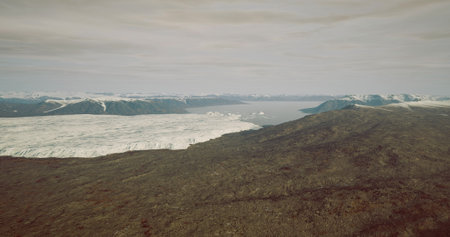 This vast landscape displays a massive glacier meeting rocky terrain under a cloudy sky. The cool...