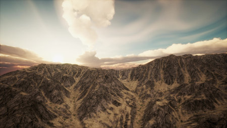Majestic mountains rise under a dramatic sky as the sun sets, casting warm light over rugged terrain. The clouds swirl above, creating a breathtaking natural spectacle of beauty.の写真素材