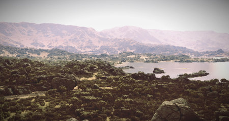 A tranquil landscape reveals a beautiful lake nestled among rolling hills and rocky formations. Lush...
