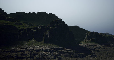 Towering cliffs create a dramatic silhouette against a soft, hazy sky. The rugged landscape near the coast showcases its natural beauty and tranquility during early evening hours.の写真素材