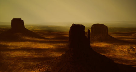 Golden hues fill the sky as the sun sets behind tall mesas in Monument Valley, Utah. The rugged terrain is marked by contrasting shadows and a peaceful atmosphere that invites reflection.の写真素材