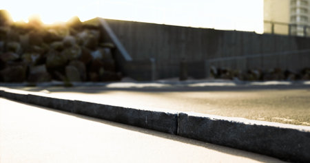 A serene urban pathway is illuminated by the warm glow of the setting sun. Shadows stretch across the pavement, while rocks are piled nearby, creating an interesting contrast.の写真素材