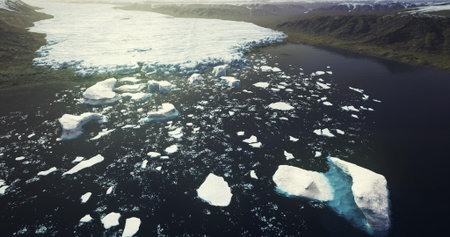 A tranquil glacial lake is dotted with large icebergs under clear skies. The scene showcases the...