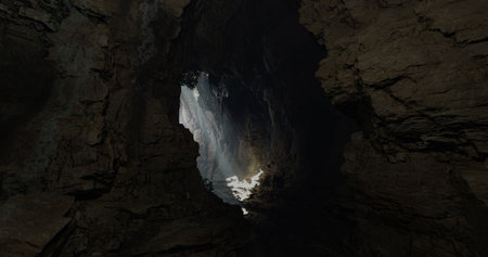 Sunlight filters through a dramatic cave opening, illuminating the rocky walls and casting soft...