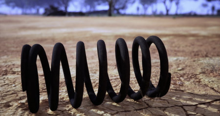 A black coil lies on parched, cracked earth in an empty landscape. Sparse trees are visible in the distance under a clear sky, suggesting a dry environment.の写真素材