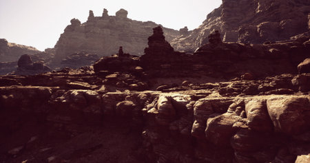 Impressive rock formations rise dramatically in a sunlit desert landscape, showcasing the rugged...