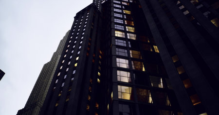 Dark skyscrapers tower against the twilight sky, with illuminated windows casting a warm glow. The...