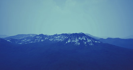 Snow capped mountain peaks rise majestically against a clear blue sky during early morning. The...
