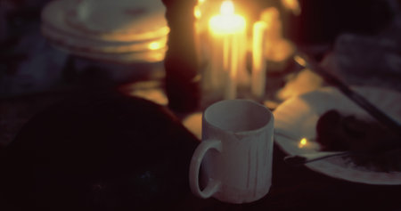 A white cup sits on a dark wooden table, illuminated by flickering candlelight. The soft glow...