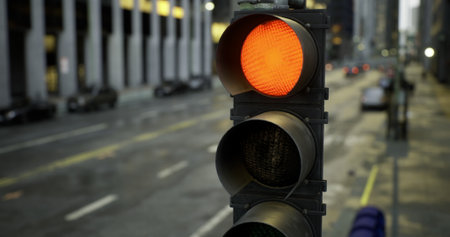 A traffic signal shows an amber light on a busy city street. Cars are parked alongside the road, and...