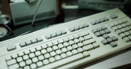 An old computer keyboard sits on a cluttered desk surrounded by various items. The keyboard shows...