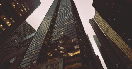 A tall, sleek skyscraper towers above nearby structures in a bustling city. The evening light reflects off the glass, creating a dramatic urban atmosphere.の写真素材