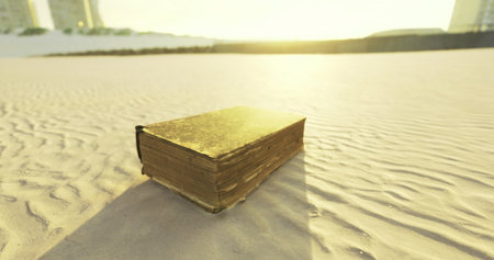 A golden colored book lies on the soft sand of a beach during sunset. The sun casts warm light, illuminating the surrounding area and highlighting the distant tall buildings.の写真素材