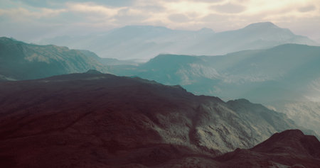 Layers of mountains stretch across the horizon under a soft dusk sky with mist enveloping the valleys. Shadows create depth in the rugged terrain, enhancing its natural beauty.の写真素材