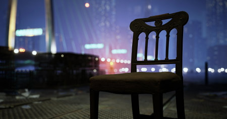 A solitary wooden chair sits by the water, illuminated by the city lights. The atmosphere is calm, with reflections of the urban skyline in the background, creating a serene night view.の写真素材