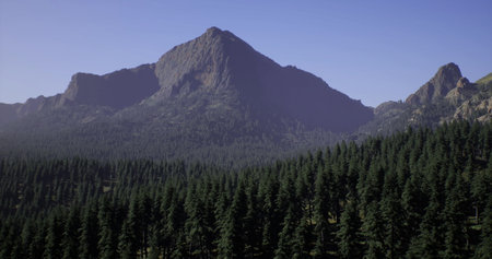 A towering mountain stands tall above a dense expanse of evergreen trees under a bright blue sky. The landscape showcases natural beauty and tranquility in a pristine environment.の写真素材