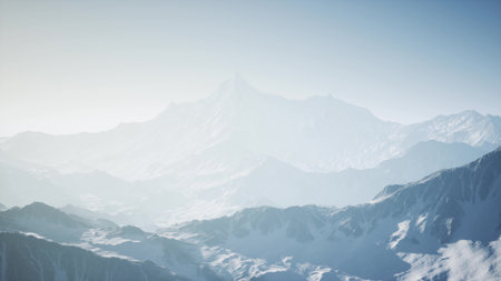 Vast mountain landscape emerges from gentle mist as dawn breaks. The soft light unveils snow capped summits and rugged terrain, evoking a sense of peace and wonder.の写真素材