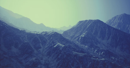 A vast mountain landscape features towering peaks and rugged terrain bathed in soft blue light during twilight. Shadows stretch across the rocky surfaces, creating depth.の写真素材