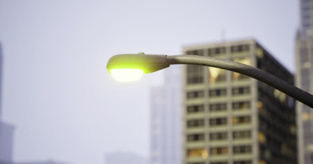 A glowing streetlight casts a warm light over sleek buildings, showcasing urban life as dusk...