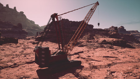 A large crane stands tall against a rugged, red rock backdrop. It is actively lifting a heavy object amidst a stark and remote terrain under clear skies, showcasing human engineering in nature.の写真素材