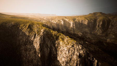 Breathtaking cliffs rise dramatically under the warm glow of the setting sun. The rugged landscape features intricate rock formations and patches of green, creating a stunning contrast.の写真素材