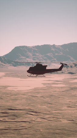 An old retro helicopter flies over a frozen lake with towering mountains in the background.