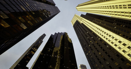 Skyscrapers tower above in a busy city, reflecting sunlight and creating a dramatic view from below....