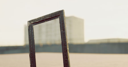 A weathered frame stands alone against a bright sky, offering a focused view of a distant urban landscape with modern buildings illuminated by the warm glow of sunset.の写真素材