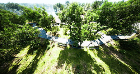A beautiful park landscape features a winding pathway surrounded by greenery. Tall trees cast long...
