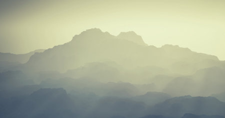 Soft layers of mist gently blanket a distant mountain range, creating a serene atmosphere. The early...