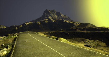 A winding road stretches toward a towering mountain, illuminated by a soft, warm light against the darkening sky. The landscape features rugged terrain and subtle shadows as dusk approaches.の写真素材