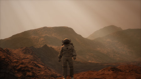 An astronaut stands on the red terrain of an unknown planet, gazing at distant mountains shrouded in mist. The atmosphere is dusty and surreal, capturing the essence of extraterrestrial exploration.の写真素材
