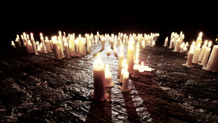 Flames dance gently atop numerous candles scattered on a rustic wooden surface. The warm glow creates a tranquil ambiance, enhancing the charm of the darkened surroundings.の写真素材