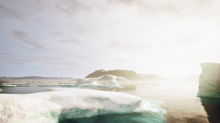 Large icebergs drift peacefully in clear waters, reflecting warm sunlight. In the background, a rugged island rises against a soft sky, creating a tranquil scene at dawn.の写真素材