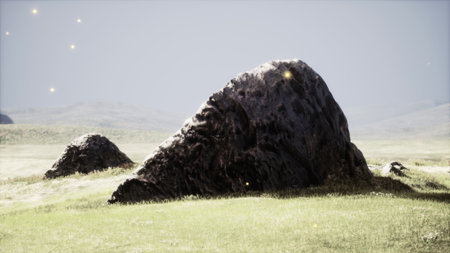 A large rock formation rests in an expansive green field, surrounded by gentle hills. Soft twinkling lights hover in the air, creating a magical atmosphere in this tranquil setting.の写真素材