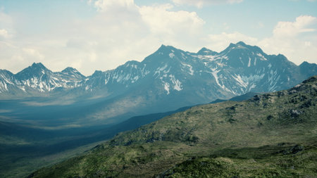Towering peaks rise dramatically against a soft blue sky, with sunlight casting shadows on lush green hills. This remote wilderness showcases natures beauty and tranquility.の写真素材