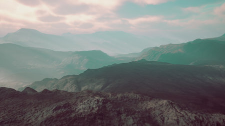 Vast mountain ranges stretch across the horizon, bathed in warm colors as the sun sets. Soft clouds drift above, creating a serene and tranquil atmosphere in the fading light.の写真素材