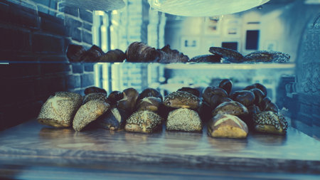 Freshly baked pastries and bread glisten under warm light in a cozy bakery. Customers gather inside,...