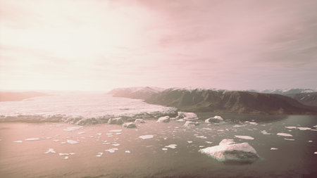 Early morning light casts a soft glow over a sweeping view of icebergs drifting in calm waters, surrounded by majestic mountains and a serene, cloud filled sky.の写真素材