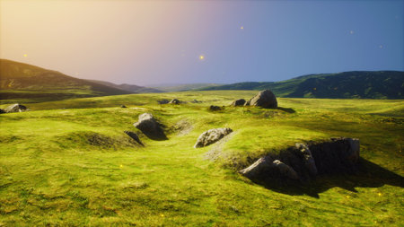Sunset bathes a wide green landscape in warm light, revealing gentle hills and rugged rocks. The tranquility of the scene invites a sense of peace and connection with nature.の写真素材