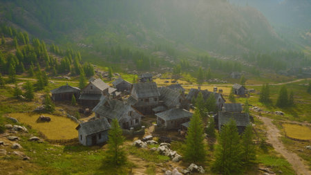 A peaceful village lies surrounded by lush trees and rugged mountains. Sunlight casts a warm glow on the old buildings, creating a serene atmosphere. Nature flourishes nearby.の写真素材