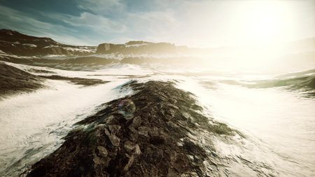 A breathtaking landscape unfolds, with rugged terrain and vast stretches of white snow. The sun casts a warm glow over distant mountains, illuminating the scenery in soft light.の写真素材