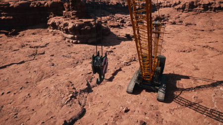A large crane, towering over the rugged terrain, is positioned in a dry desert setting. Its mechanical arm reaches down, ready to lift heavy materials from the arid ground.の写真素材