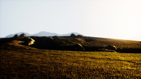 Golden sunlight spills over rolling hills as large boulders dot the foreground. The serene setting captures the peaceful essence of nature during dusk, inviting contemplation and tranquility.の写真素材