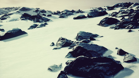 A serene winter landscape showcases dark rocks protruding through a thick layer of soft snow, set...