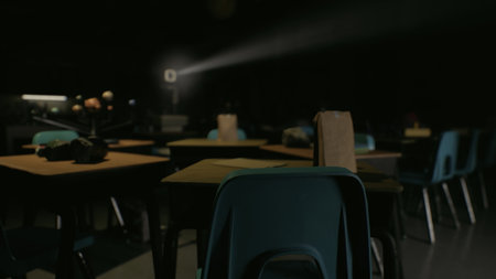 Empty desks fill the dimly lit classroom while a beam of light from a projector cuts through the darkness, creating a mysterious ambiance that invites imagination.の写真素材