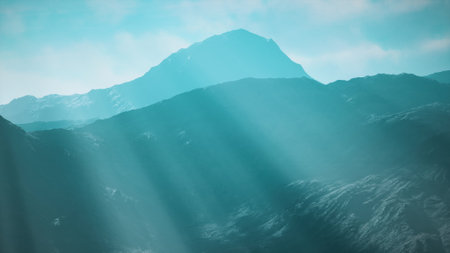 A breathtaking mountain range stands tall under a soft blue sky. Sunlight streams through the peaks, highlighting the serene beauty of the rugged terrain. A moment of tranquility unfolds.の写真素材